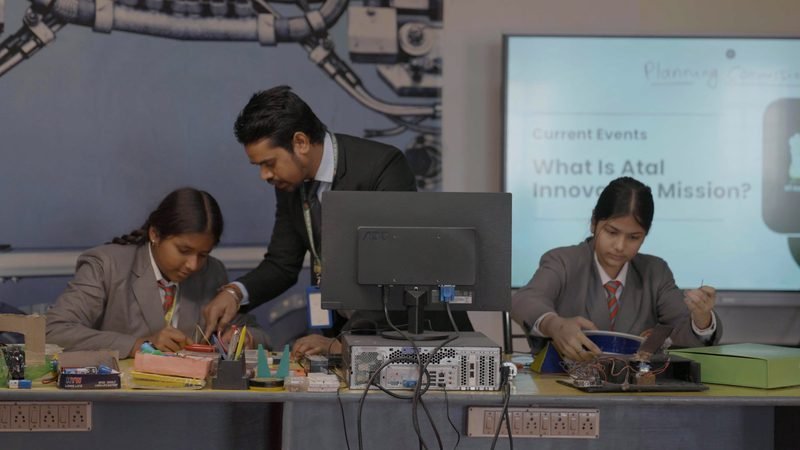 A teacher guiding two students at the robotics and electronics bench
