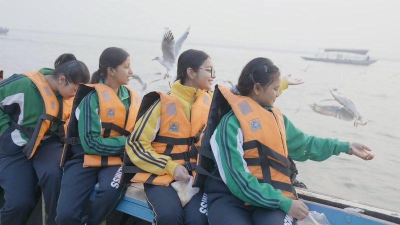 Students reaching out to the gulls from a boat on the Ganga