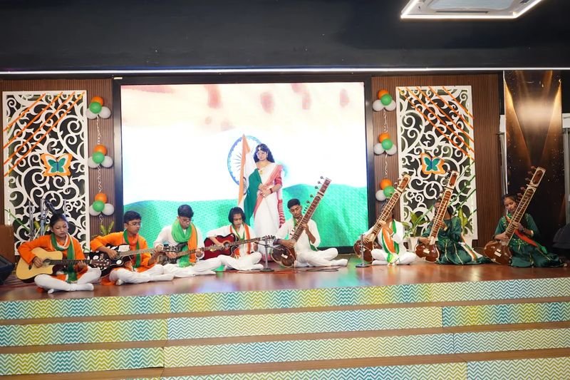 Students playing guitars and Indian classical instruments on stage